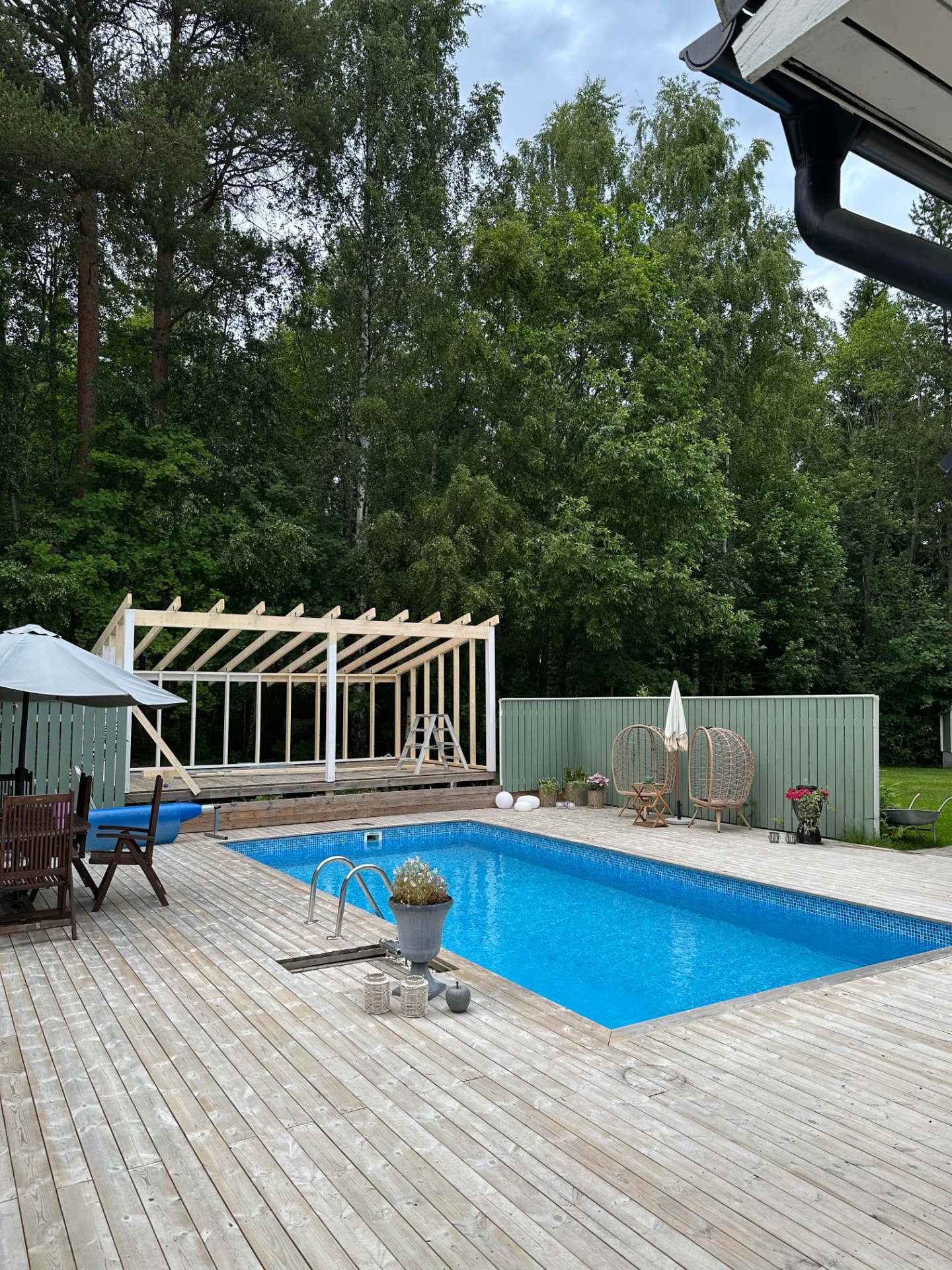 Poolhus under byggnation med trädäck och pool i trädgården